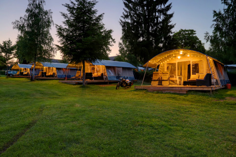 Aftenbillede af oplyste glamping telte og terrasseområder på Auf Kengert feriepark i Diekirch, Luxembourg.