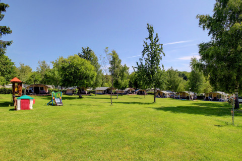 Terrain de camping verdoyant avec tentes, aire de jeux et arbres au parc Auf Kengert à Diekirch, Luxembourg.