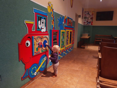 Toddler plays with a colorful train-shaped wall activity panel at Auf Kengert holiday park in Diekirch, Luxembourg.