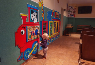Lille barn leger med interaktivt vægpanel formet som tog på et legeområde i Auf Kengert, Diekirch, Luxembourg.
