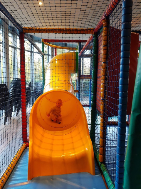 Un bambino piccolo gioca su uno scivolo giallo al coperto al parco vacanze Auf Kengert di Diekirch.