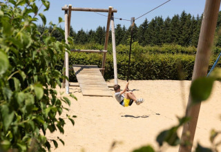 Niño jugando en una tirolesa en un parque infantil rodeado de árboles en Auf Kengert, Diekirch, Luxemburgo.