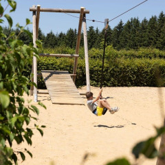 Ragazzo gioca su una zipline nel parco giochi circondato da alberi ad Auf Kengert, Diekirch, Lussemburgo.