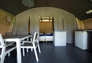 Interior view of a luxury tent at Auf Kengert holiday park in Diekirch, Luxembourg, with dining table and beds.