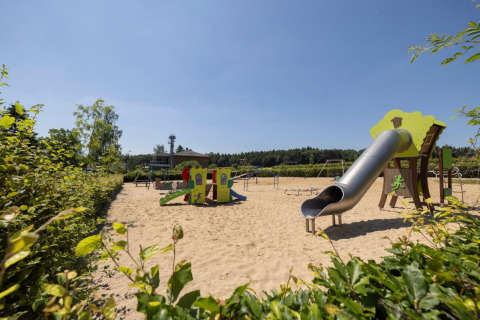 Parco giochi con scivolo e area sabbiosa presso il villaggio Auf Kengert a Diekirch, Lussemburgo, in una giornata soleggiata.