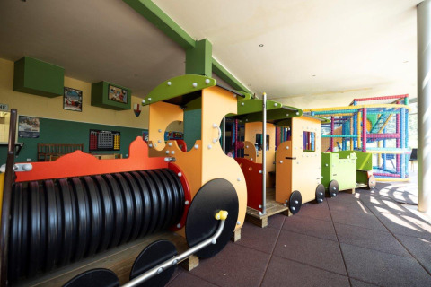 Parque infantil interior con tren de juguete colorido y estructura de escalada en Auf Kengert, Diekirch, Luxemburgo.