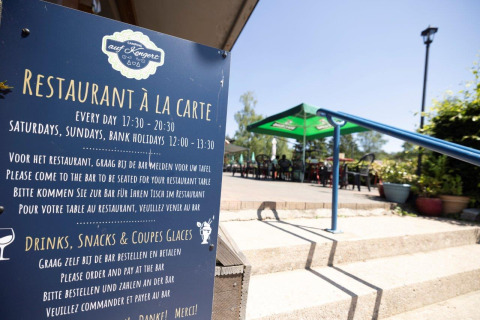 Outdoor restaurant terrace at Auf Kengert holiday park in Diekirch, Luxembourg, with hours sign in view.