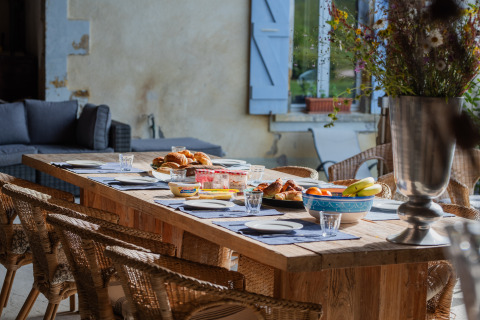 Outdoor breakfast table with croissants, fruit, and flowers at Domaine La Barbe holiday park in Occitanie, France.