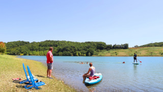 Visitors enjoy paddleboarding and relaxing by the lake at Domaine La Barbe holiday park in Occitanie.