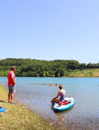 Visitors enjoy paddleboarding and relaxing by the lake at Domaine La Barbe holiday park in Occitanie.