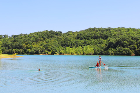 People paddle boarding and swimming on a lake surrounded by green hills at Domaine La Barbe, Occitanie, France.