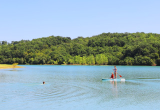 Persone fanno paddle e nuotano in un lago circondato da colline verdi a Domaine La Barbe, Occitania, Francia.