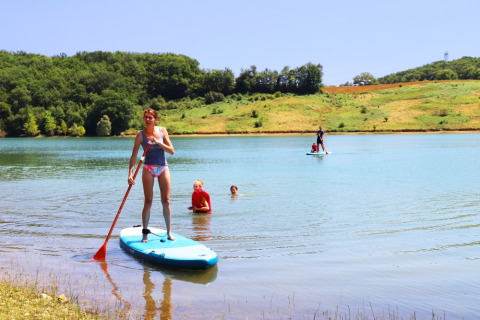 Mujer en paddle surf y niños nadando en el lago de Domaine La Barbe, Occitanie, Francia.