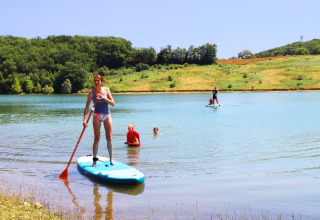 Vrouw op paddleboard, kinderen zwemmen in het meer bij Domaine La Barbe, Occitanie, Frankrijk.