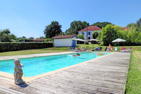 Außenpool im Domaine La Barbe Ferienpark in Okzitanien, Frankreich, mit Erholungsgästen und Häusern im Hintergrund.
