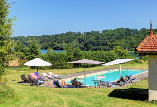 Outdoor pool with sun loungers, umbrellas, and greenery at Domaine La Barbe holiday park in Occitanie, France.