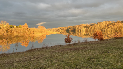Peaceful lake landscape at Domaine La Barbe, Occitanie, France, with golden trees and glassy water reflection.