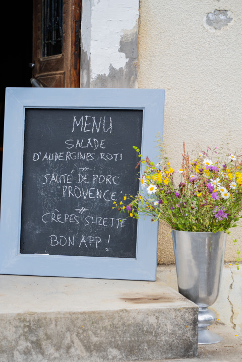 Menu tavle med fransk tekst ved siden af en vase med vilde blomster, Domaine La Barbe, Occitanie, Frankrig.