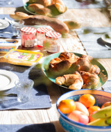 Outdoor breakfast table near Lalanne-Arqué, Occitanie, with croissants, fruit bowl, jams, and fresh bread.