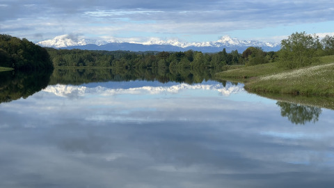 Serene lake at Domaine La Barbe holiday park in Occitanie, France with snowy mountains and reflection in water.