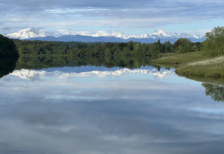 Rolig sø ved Domaine La Barbe i Occitanie, Frankrig, med spejlblankt vand og sneklædte bjerge i baggrunden.