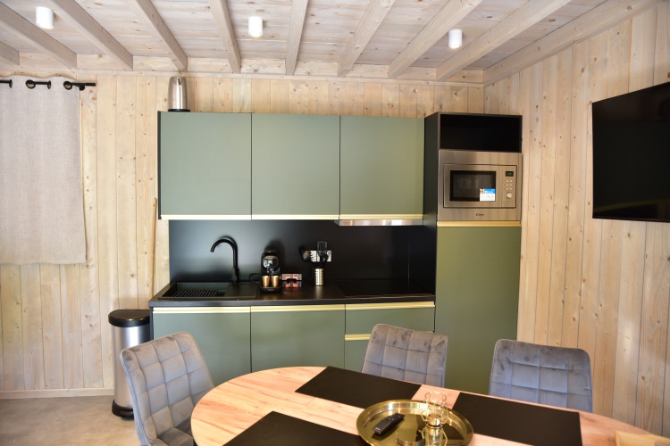 Moderne Küchenbereich in der Ecolodge im Hameau de l'Ourthe, Belgien, mit grünen Schränken und Tisch.