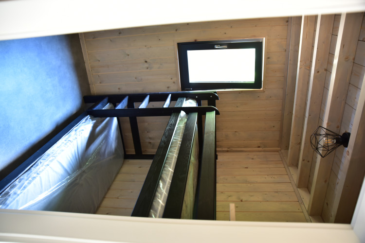 View of a loft bed with a window and wooden walls inside the Ecolodge at Hameau de l'Ourthe in Belgium.