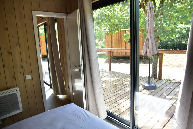 Blick aus dem Schlafzimmer einer Ecolodge mit Zugang zur Holzterrasse und Waldlandschaft draußen.
