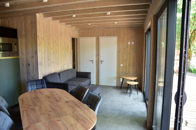 Vue intérieure d'une Ecolodge au Hameau de l'Ourthe en Belgique, avec panneaux de bois, canapé et table.