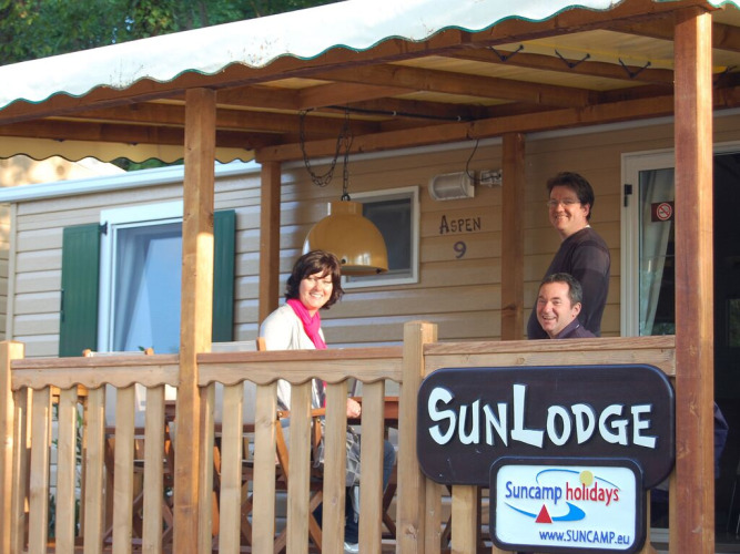 Tres personas sentadas en el porche de SunLodge Aspen en Altomincio Family Park, Italia, sonriendo.