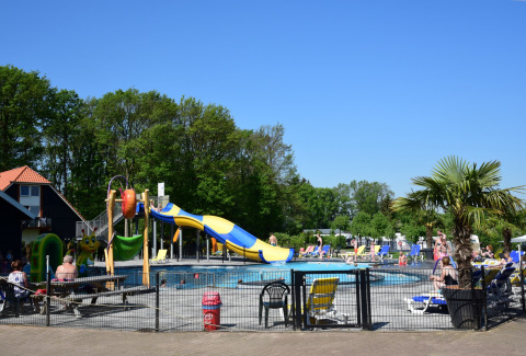 Buitenzwembad met glijbaan en zonnebedden bij Camping de Koeksebelt, Overijssel, op een zonnige dag.