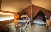 Inde i et Classic Tent ved Huttopia Fontvieille, Frankrig, med senge, bord, stole og opbevaring.