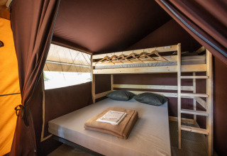 Interiør af et klassisk safaritelt på Huttopia Fontvieille i Frankrig med dobbeltseng og køjeseng.