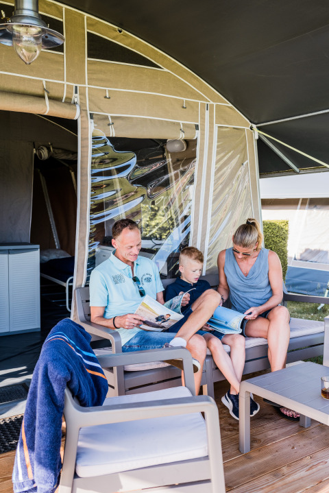 Family relaxing and reading magazines together on the terrace at Auf Kengert Lodge de Luxe in Luxembourg.