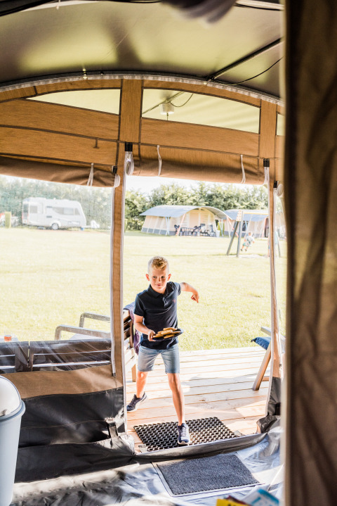 Ragazzo entra nell' Auf Kengert Lodge de Luxe in Lussemburgo, tiene del cibo, tende e caravan fuori.