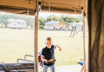 Ragazzo entra nell' Auf Kengert Lodge de Luxe in Lussemburgo, tiene del cibo, tende e caravan fuori.