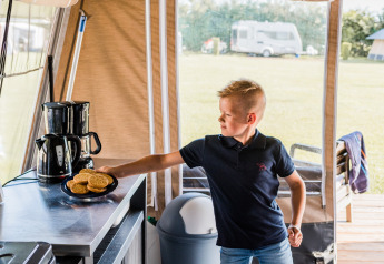 Jongen pakt koekjes in een tentkeuken bij Auf Kengert Lodge de Luxe in Luxemburg, camping op de achtergrond.