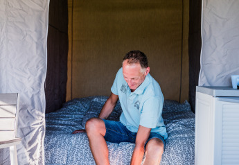 Hombre sentado en una cama en Auf Kengert Lodge de Luxe en Luxemburgo, poniéndose los zapatos en la habitación.