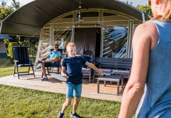 Jongen speelt met een vrouw buiten Auf Kengert Lodge de Luxe in Luxemburg, man ontspant op de achtergrond.