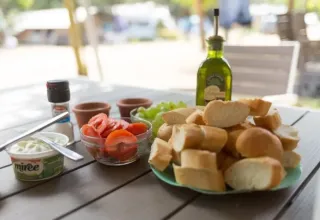Outdoor table with fresh baguette, tomatoes, grapes, olive oil, and cheese spread at Camping Le Clou, France.