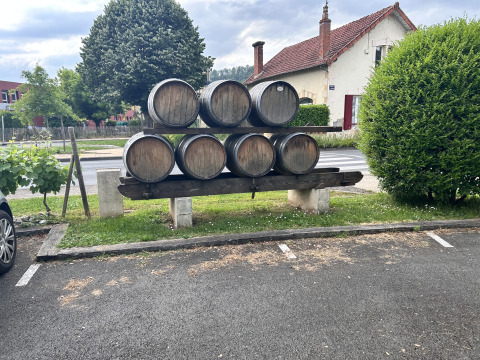 Wood barrels stacked outdoors by a house at Camping Le Clou in Nouvelle-Aquitaine, France, near a parking area.