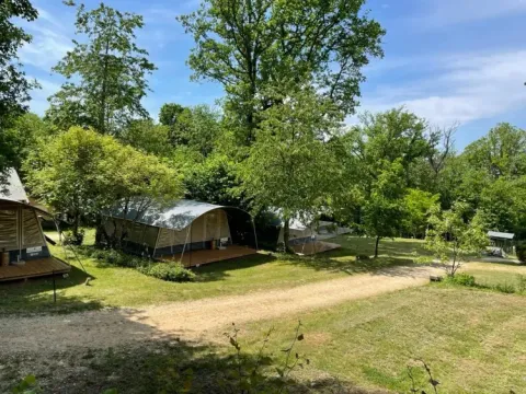 Tented lodges surrounded by trees at Camping Le Clou holiday park in Nouvelle-Aquitaine, France, on a sunny day.