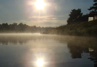 Ochtendzon schijnt boven mistige rivier bij Camping de Koeksebelt in Overijssel, Nederland, met reflectie op het water.