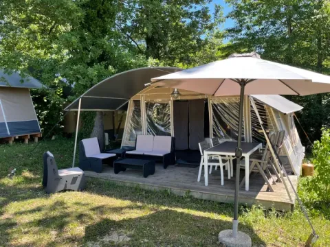 Tienda glamping equipada en Camping Le Clou, Nouvelle-Aquitaine, Francia, con terraza y sombrilla al aire libre.