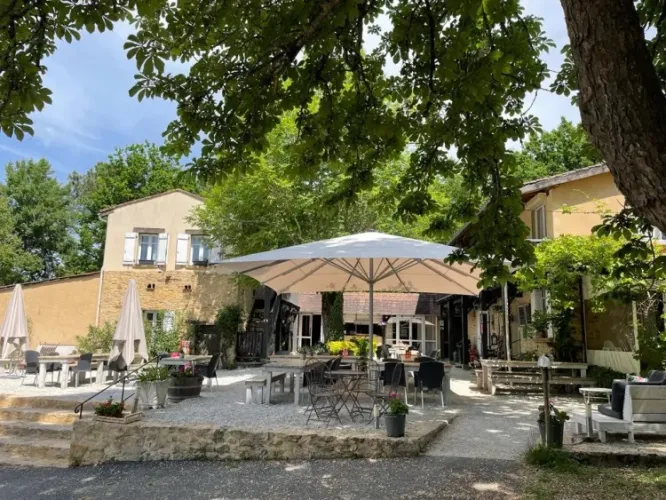 Buitenruimte met tafels, stoelen en parasols bij Camping Le Clou, vakantiepark in Nouvelle-Aquitaine, Frankrijk.