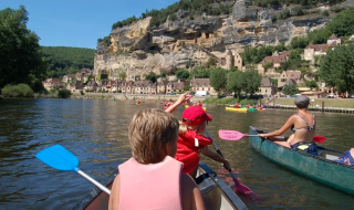 Persone in canoa su un fiume davanti a case di pietra e scogliere a Nouvelle-Aquitaine, Francia.