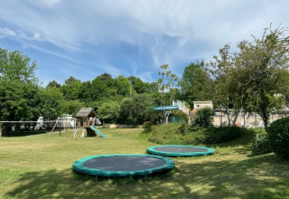 Area giochi con tappeti elastici, altalene e scivolo al Camping Le Clou in Nouvelle-Aquitaine, Francia.