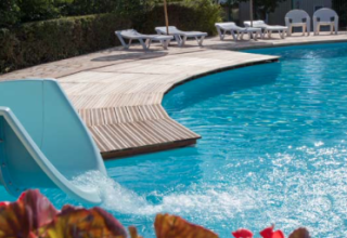 Outdoor pool with a waterslide, loungers, and umbrellas at Camping Le Clou in Nouvelle-Aquitaine, France.