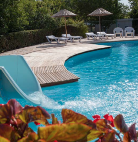 Outdoor pool with a waterslide, loungers, and umbrellas at Camping Le Clou in Nouvelle-Aquitaine, France.
