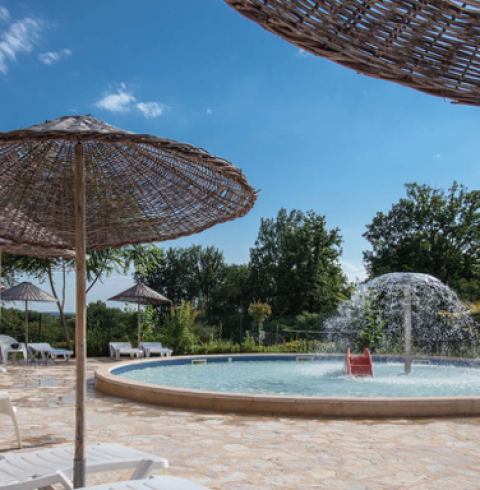 Rond zwembad met fontein en rieten parasols bij Camping Le Clou, Nouvelle-Aquitaine, Frankrijk.